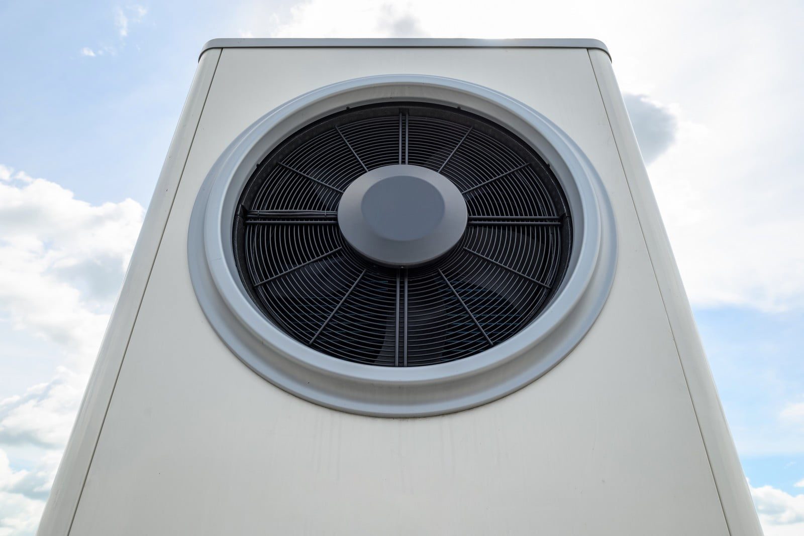 This image shows an outdoor unit of an HVAC system, commonly known as an air conditioner (AC) condenser unit. The unit is installed outside and is a critical part of an air conditioning system, which releases heat from the refrigerant into the atmosphere to cool down the indoor air. The large fan visible in the centre of the unit is used to circulate air across the condenser coils to dissipate the heat. The sky in the background indicates that the photo was taken outside during the day.