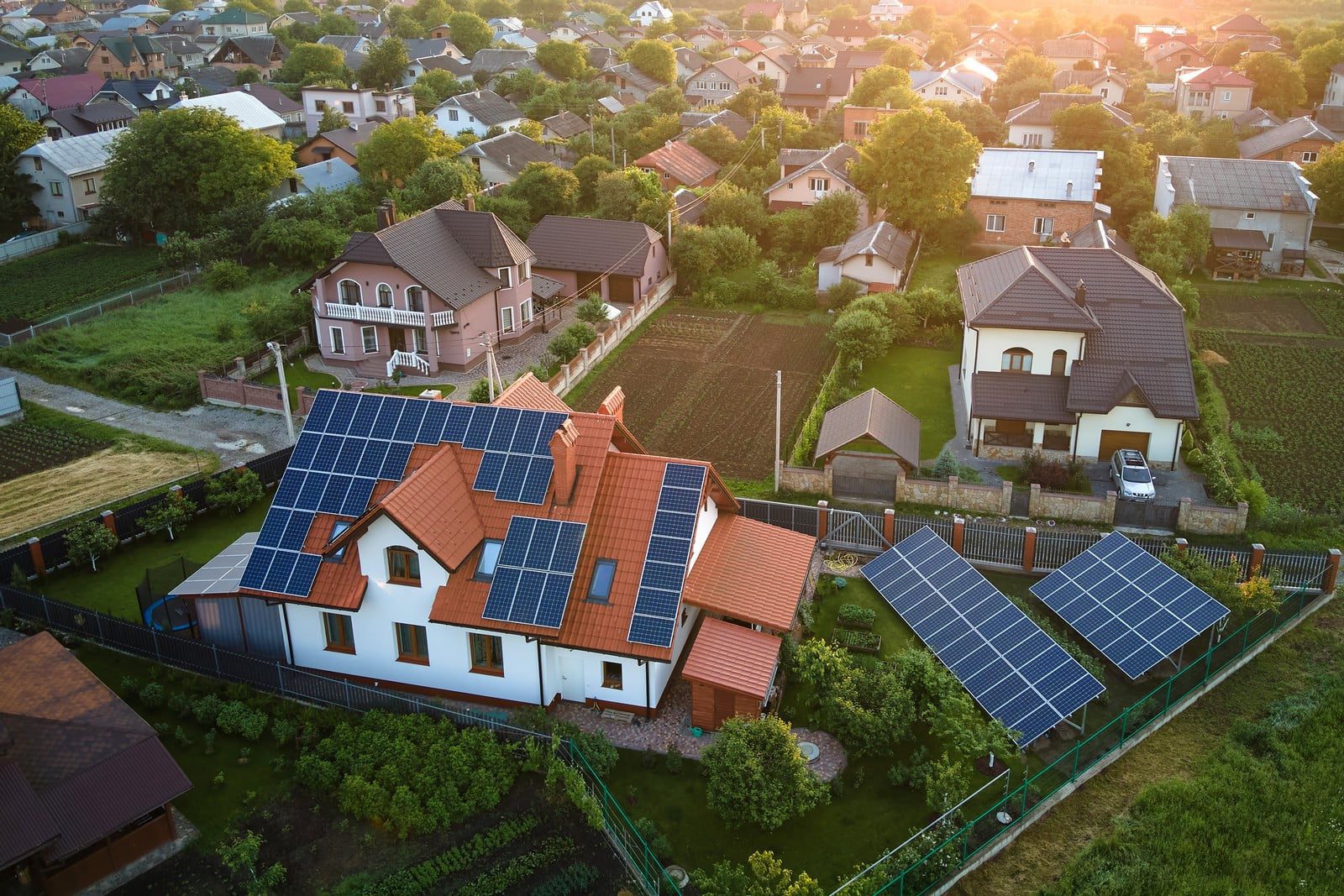 The image depicts a private home with a modern, well-maintained roof covered in solar photovoltaic panels. The house appears to be situated in a residential neighborhood, surrounded by lush greenery and mature trees. The roof is gabled and has a dark, sleek finish that complements the shiny, blue-tinted solar panels. The panels are arranged in neat, parallel rows, maximising the roof space to capture solar energy efficiently. There are no visible cables or mounting hardware, giving the installation a seamless, integrated look. The sky above is clear with a bright, sunny atmosphere, suggesting optimal conditions for solar energy production. The overall appearance is clean and eco-friendly, reflecting a commitment to sustainable living.